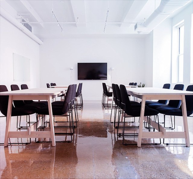 Blick in einen Seminarraum mit Tisch, Stühlen und einem großen Bildschirm an der Wand.