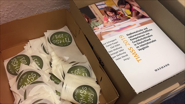 Blick in zwei Kartons hinein, in denen die TIMSS-Publikation sowie Aufkleber liegen.